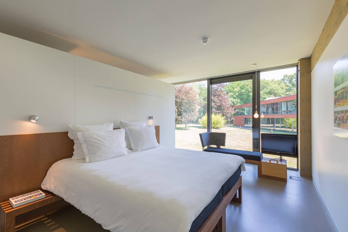 A modern hotel room with a large bed, a television, and a view of the outdoors.