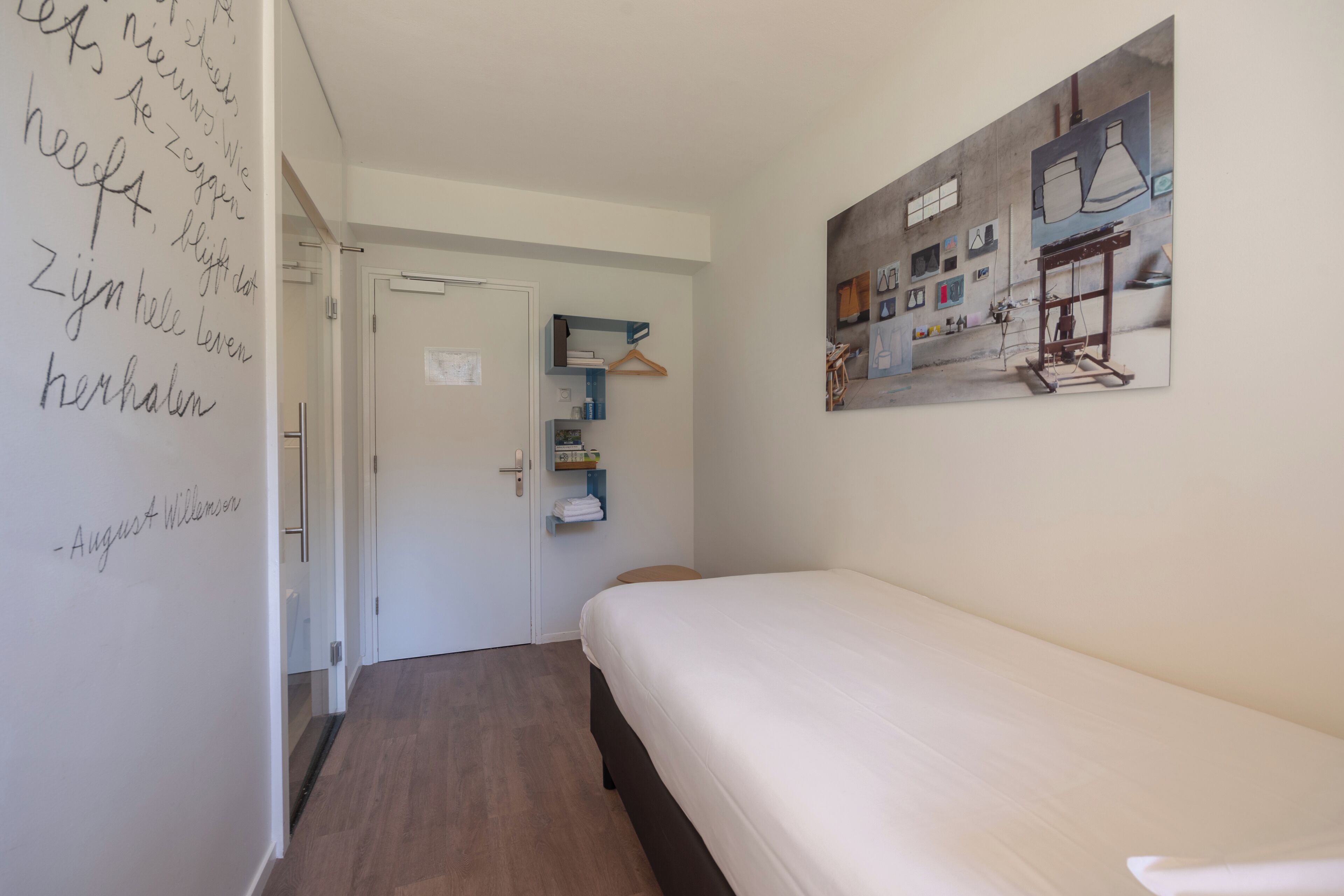 A bedroom with a bed, a door leading to a bathroom, and a wall with a painting.