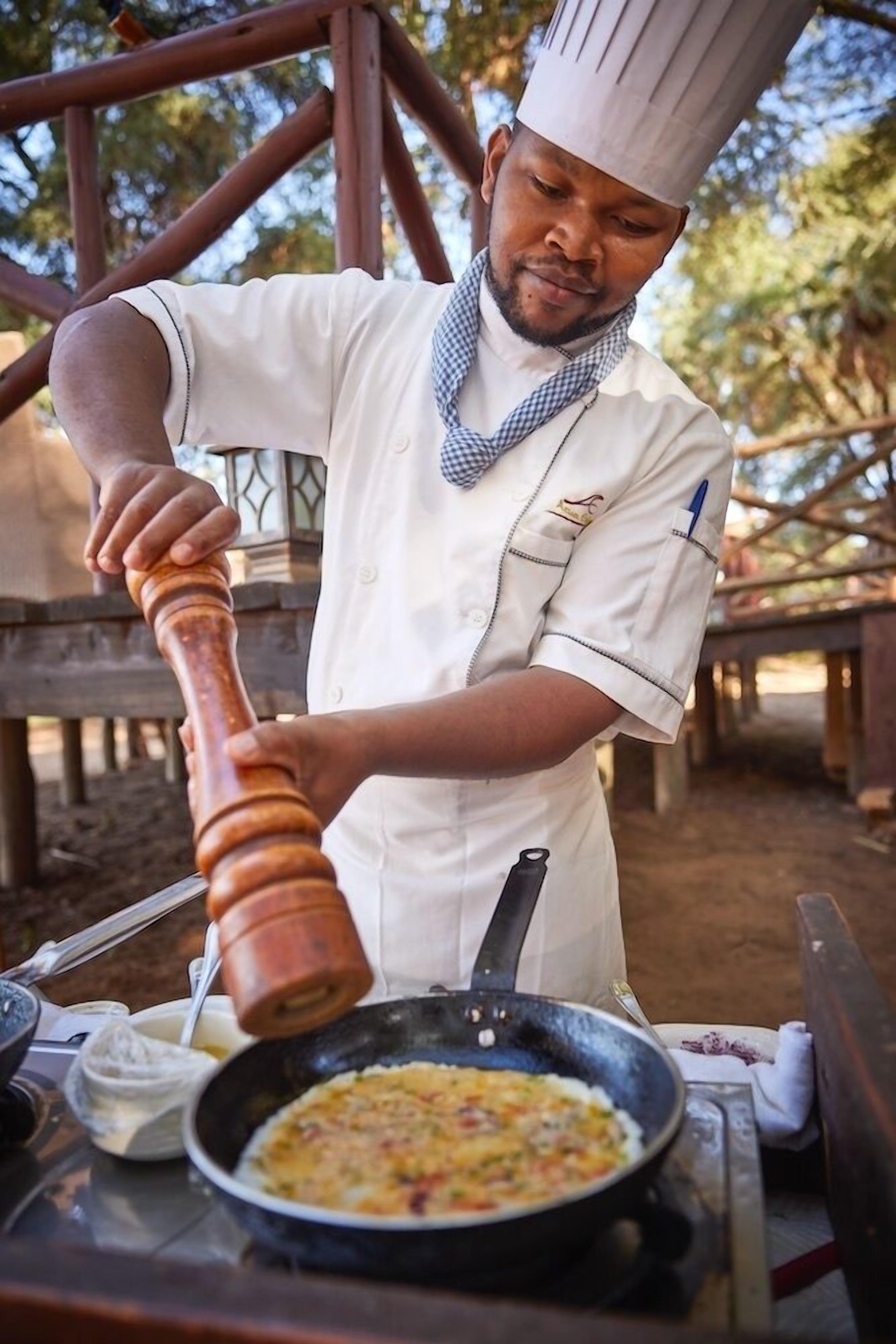 Un cocinero con uniforme blanco y gorro de chef, preparando comida en una sartén.