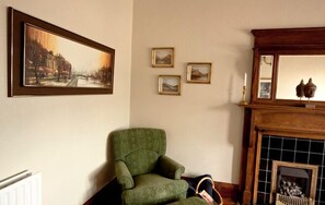 A room with a green armchair, a fireplace, and three framed pictures on the wall. - Cloudberry Apartment (Edinburgh)