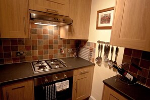 A kitchen with wooden cabinets, a gas stove, a tiled backsplash, and hanging utensils. - Cloudberry Apartment (Edinburgh)