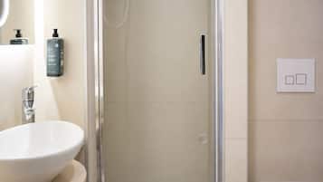 Un baño moderno con ducha envuelta en vidrio, un lavamanos blanco y un inodoro.