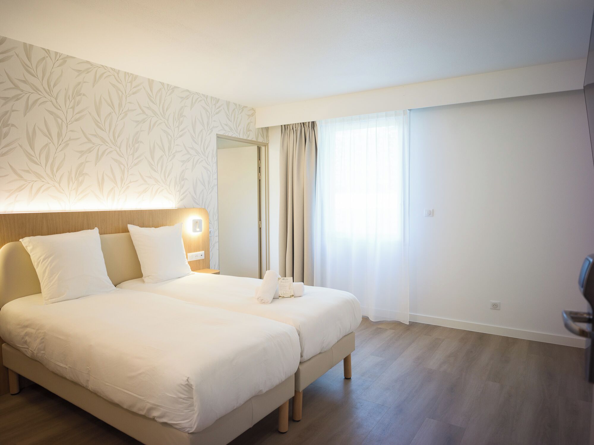 Une chambre d’hôtel avec un grand lit, une table de chevet, un miroir et une fenêtre avec des rideaux.