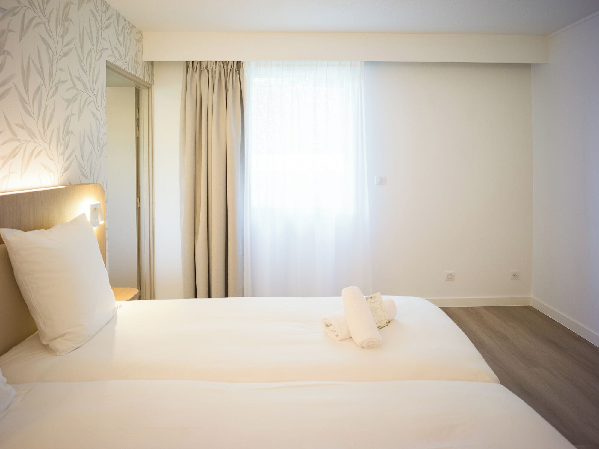 Una habitación de hotel con una cama grande, una lámpara de noche y un ventanal con cortinas.
