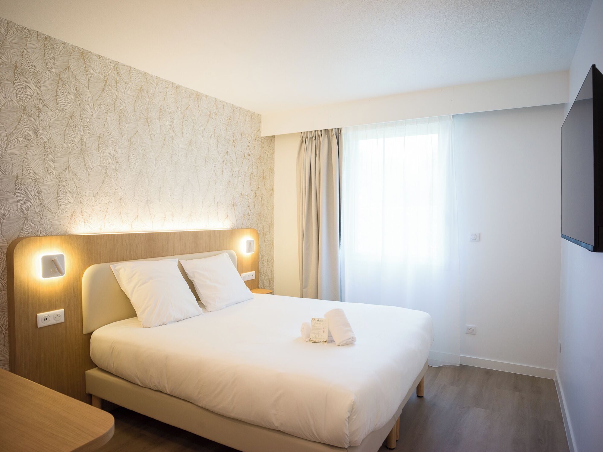 A hotel room with a bed, bedside table, and a wall-mounted TV.
