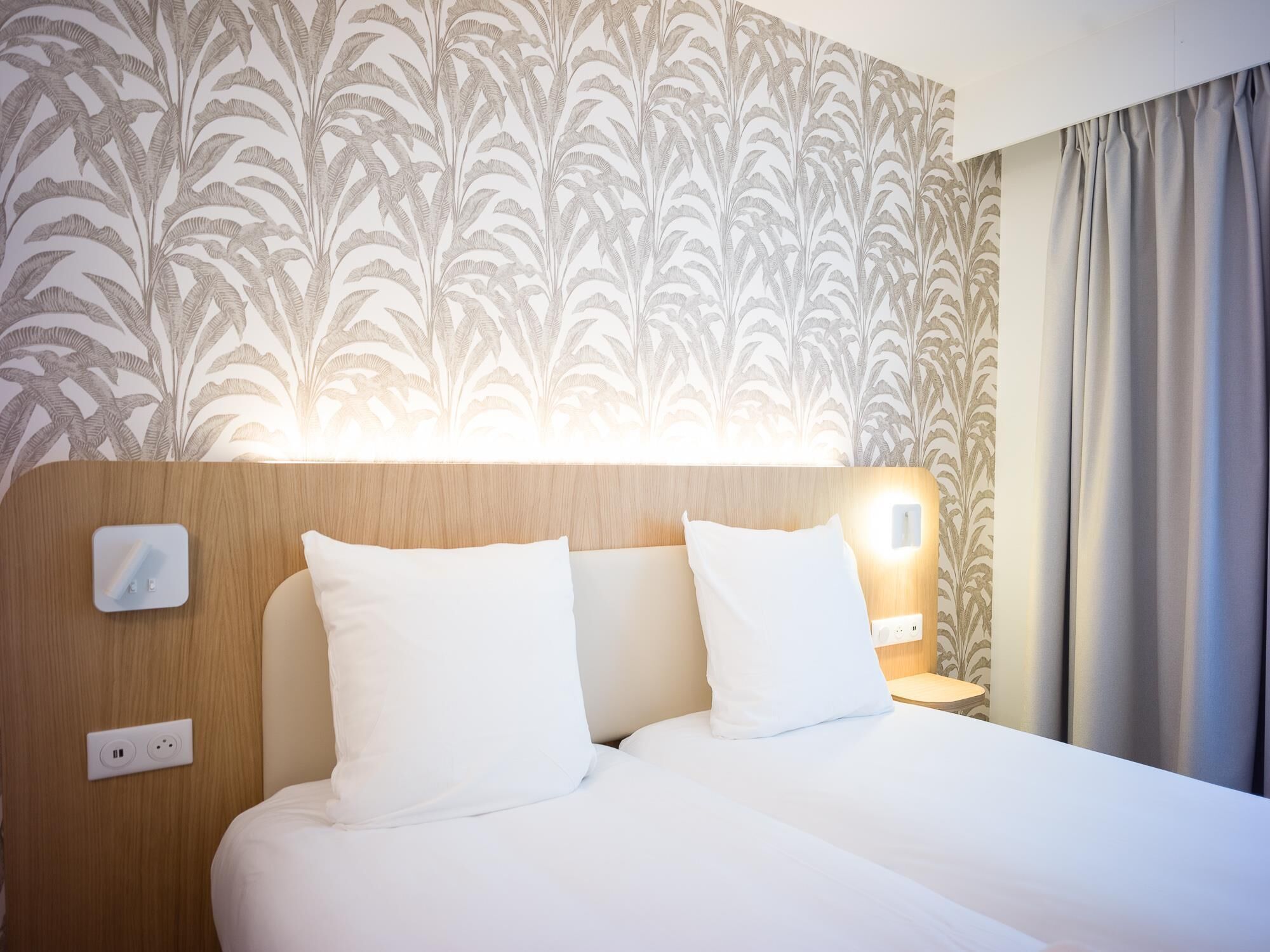 Habitación de hotel con cama, dos lámparas de noche, un enchufe y una pared con diseño de hojas.