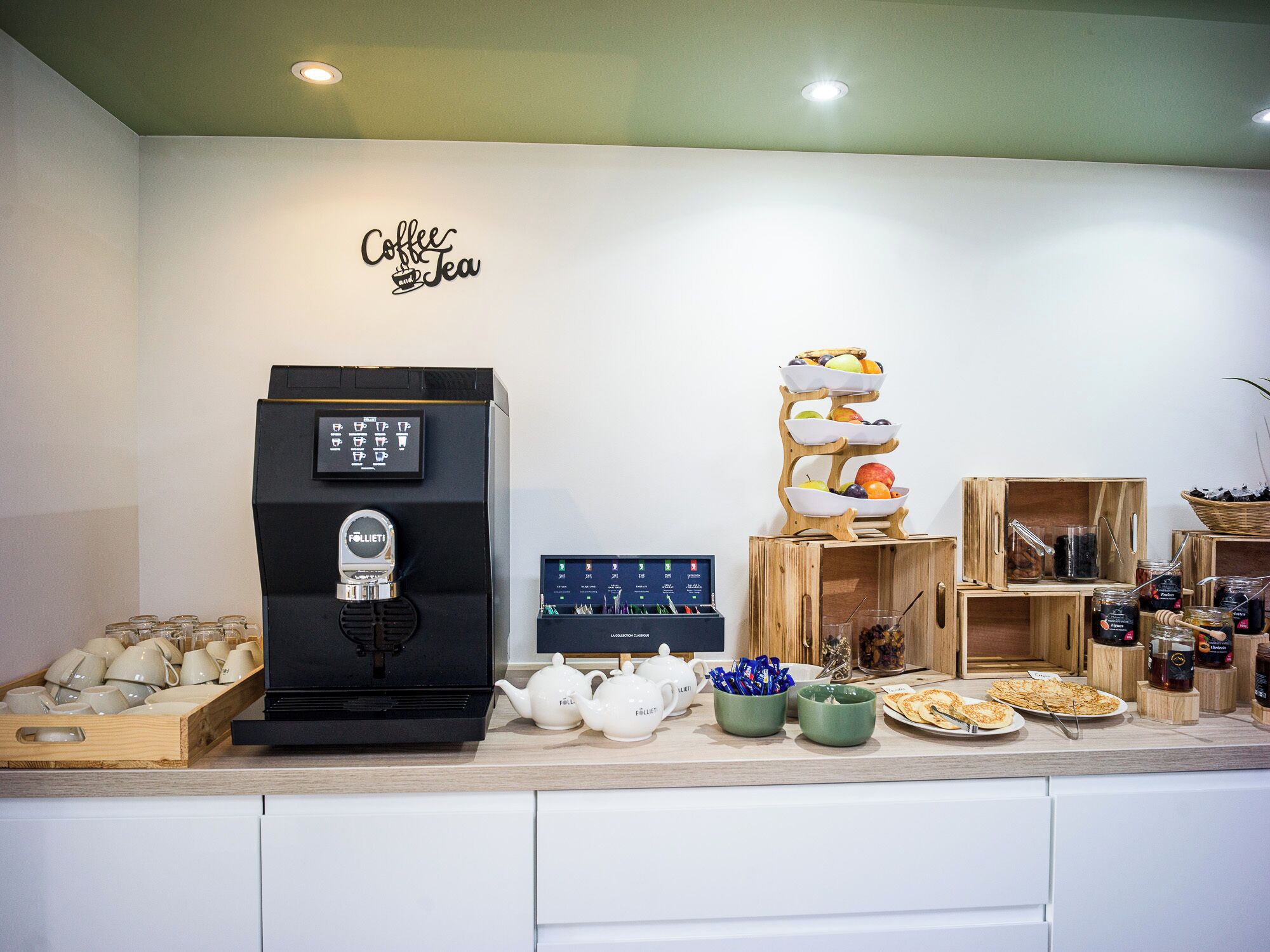 A coffee and tea station with a coffee machine, teapots, a fruit display, and various jars of condiments.