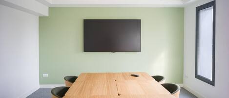 Uma sala de conferências com uma mesa comprida, quatro cadeiras, uma TV de tela plana na parede e uma janela grande.
