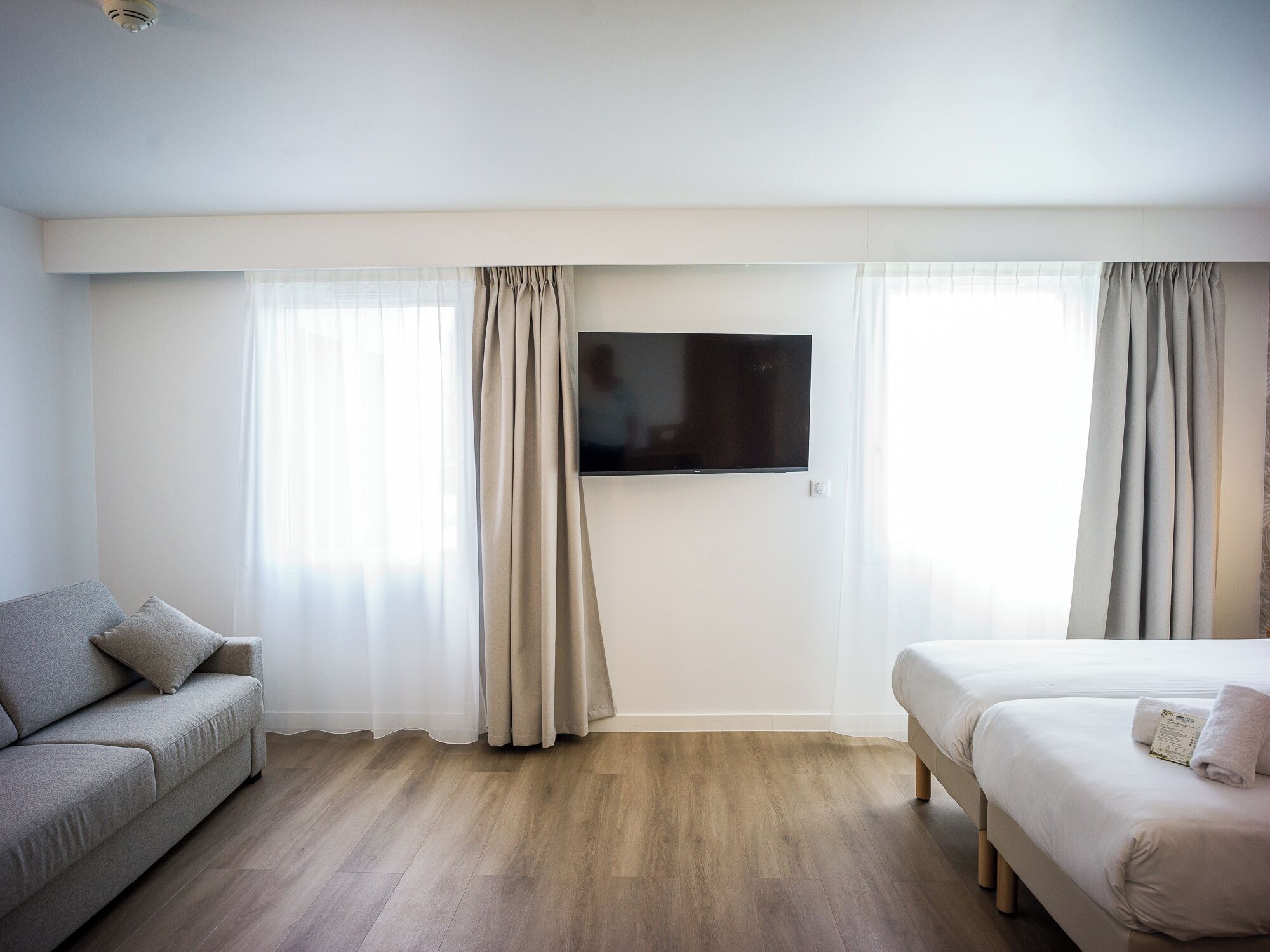 Une chambre d’hôtel avec un lit, un canapé, un téléviseur à écran plat fixé au mur et un plancher en bois.