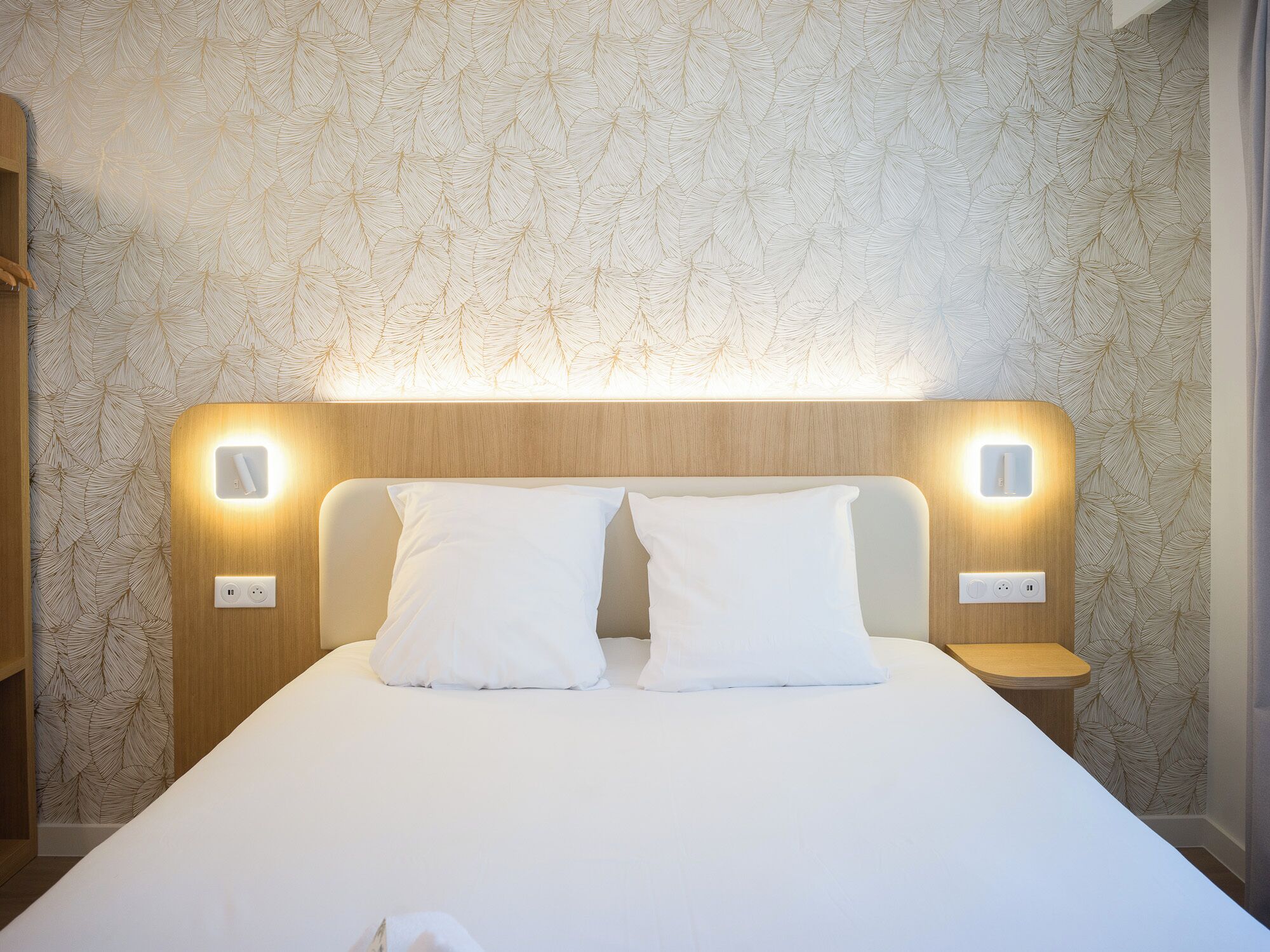 Una habitación de hotel con una cama grande, dos mesitas de noche y una pared con diseño de hojas.