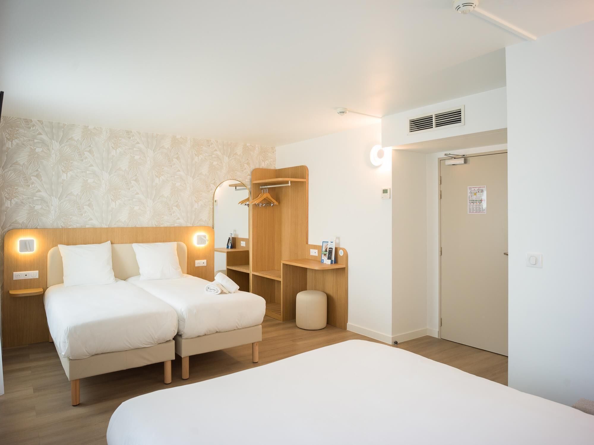 Ein Hotelzimmer mit zwei Betten, einem Holzschrank, einem Spiegel und einem kleinen Hocker.