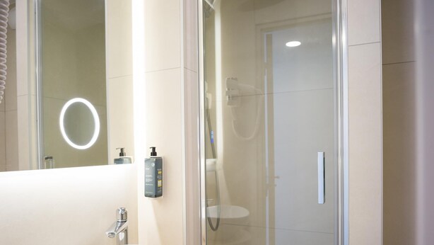 Een moderne badkamer met een witte wastafel, een douchecabine van glas en een spiegel met rondom verlichting.