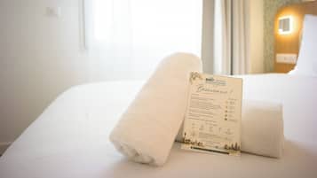 Een hotelkamer met een net opgemaakt bed, een welkomstbord en een raam met gordijnen.