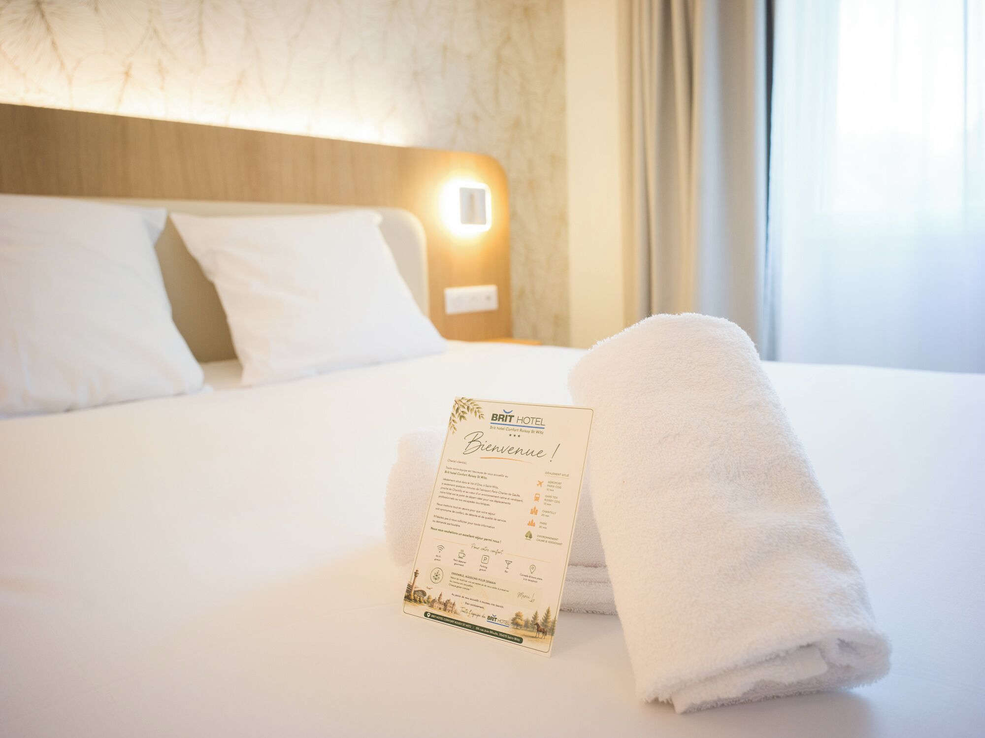 A neatly made hotel bed with a white towel and a welcome card.