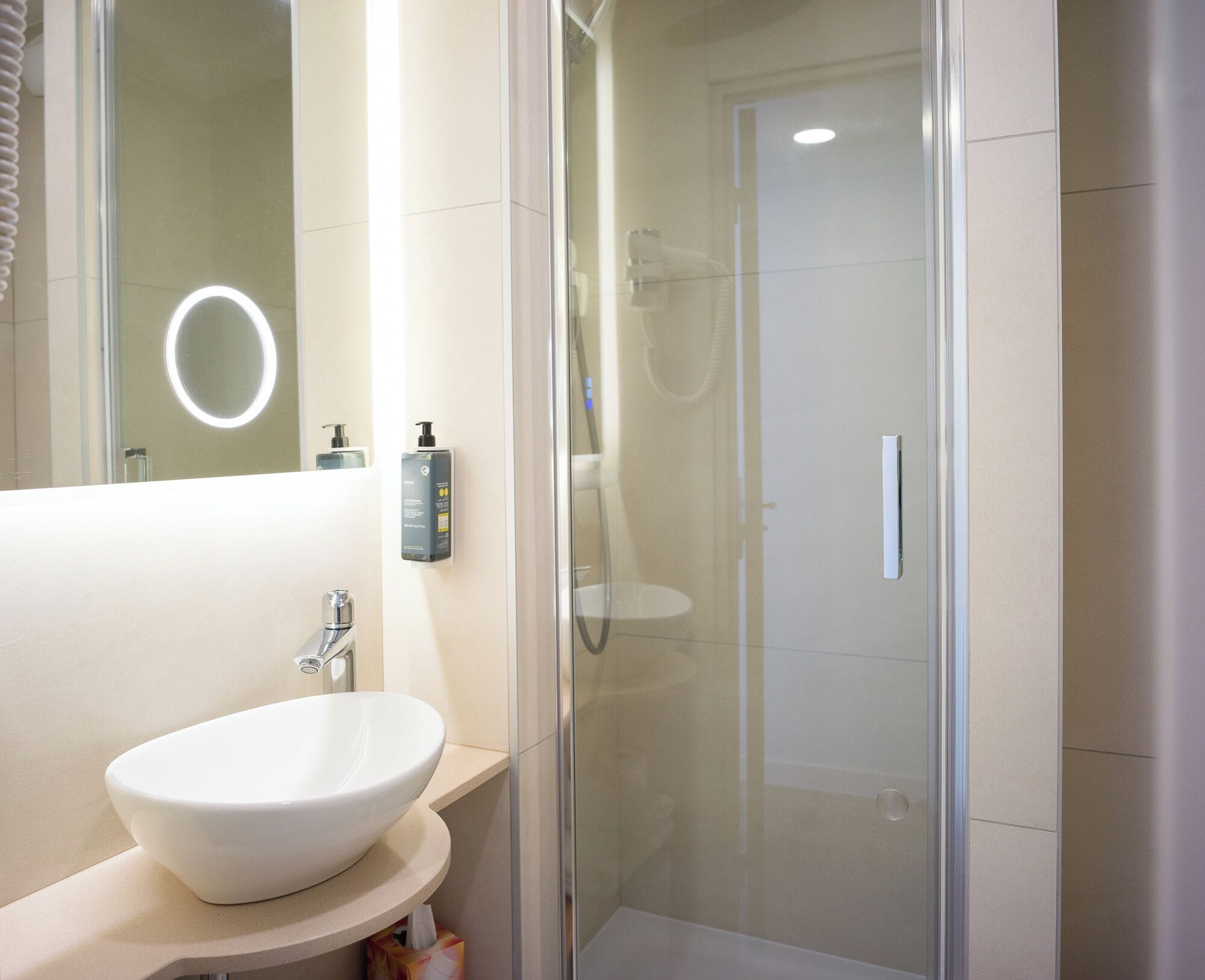 A modern bathroom with a white sink, a mirror, and a glass-enclosed shower.