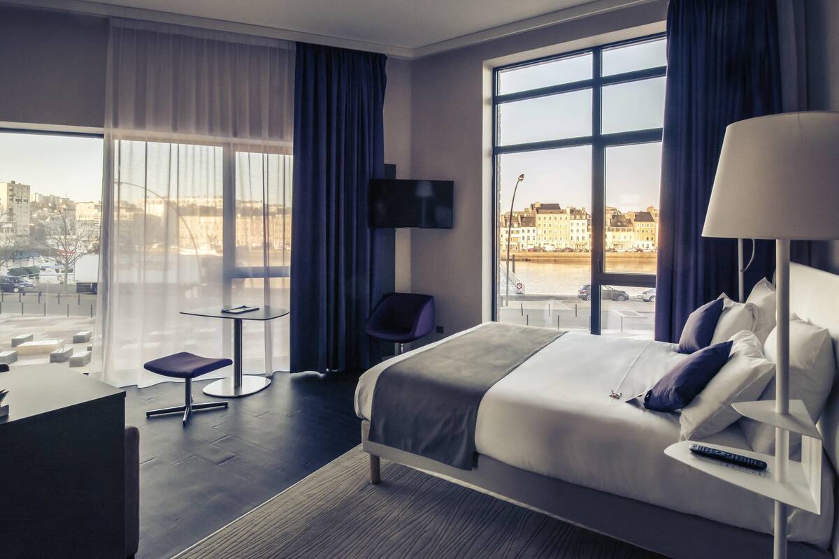 A modern hotel room with a large bed, a desk, a chair, and a TV.