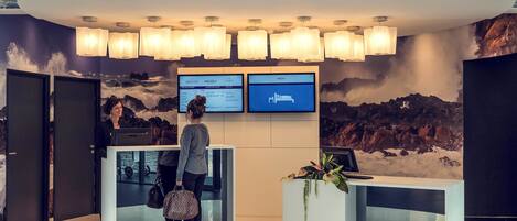 A reception area with a modern design, featuring a curved reception desk, multiple screens displaying information, and a mountainous mural on the wall.