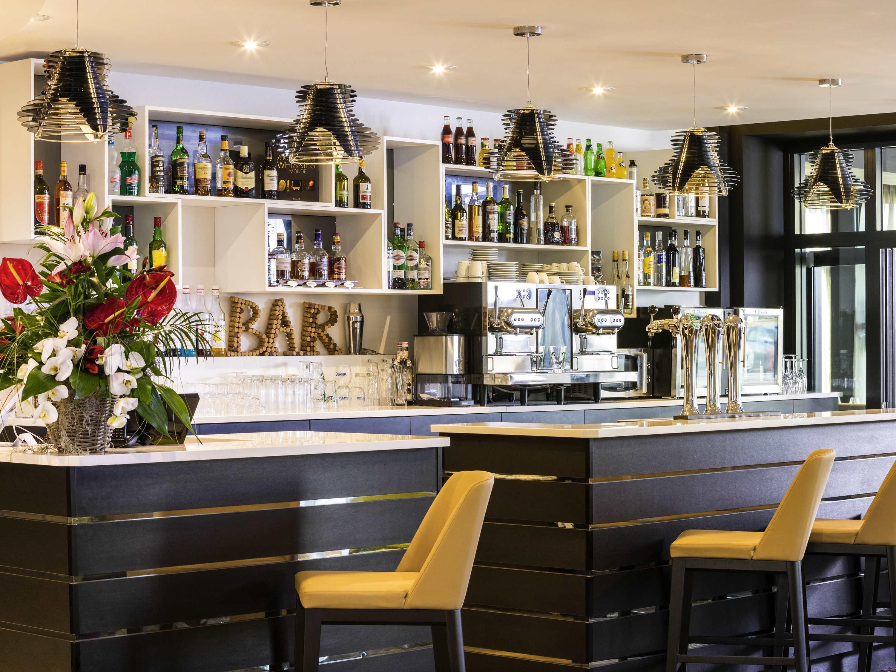 Zona de bar con mostrador, taburetes, estanterías llenas de botellas y un letrero decorativo que dice 'BAR' hecho con botellas.
