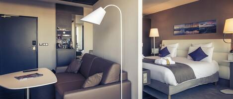 A modern hotel room with a sofa, a bed, a desk, and a lamp.