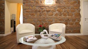 A lobby with a stone wall, two white armchairs, a glass coffee table with books and a decorative swan, and a 'HELLO' sign. - Freedom Love B&B (Rome)
