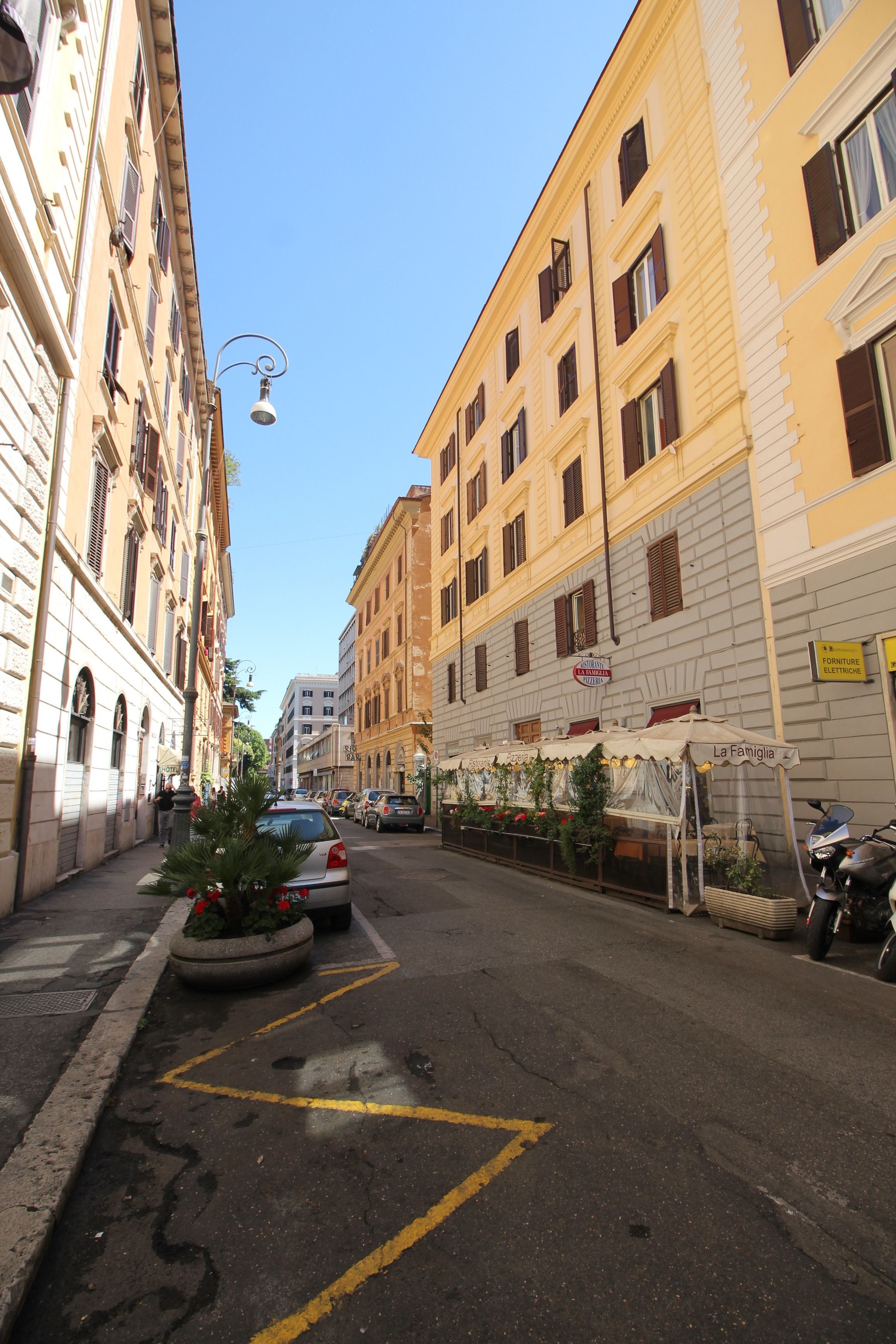 A narrow street with parked cars, a Christmas tree, and a building with a sign reading "La Famiglia".