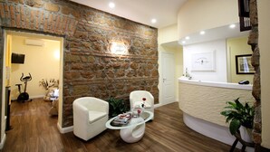 A reception area with a stone wall, a reception desk, white chairs, and a coffee table with magazines and a vase. - Freedom Love B&B (Rome)