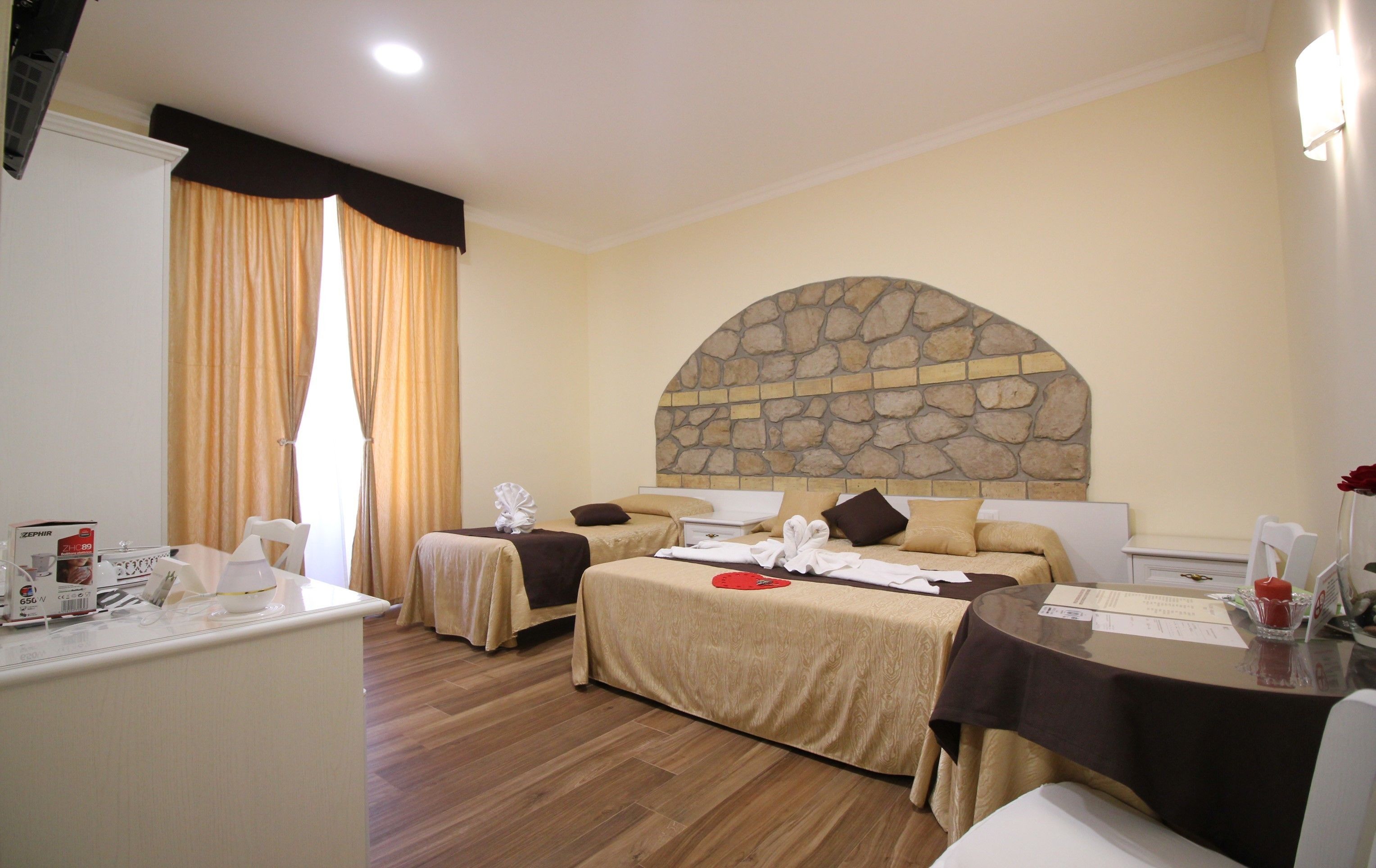 Une chambre d’hôtel avec deux lits, un mur en arc de pierre, un plancher en bois et un bureau avec une chaise.