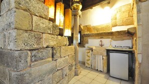 A rustic kitchen with stone walls, a wooden ceiling, a sink, a refrigerator, and hanging lights. - Felline In B&B (Alliste)