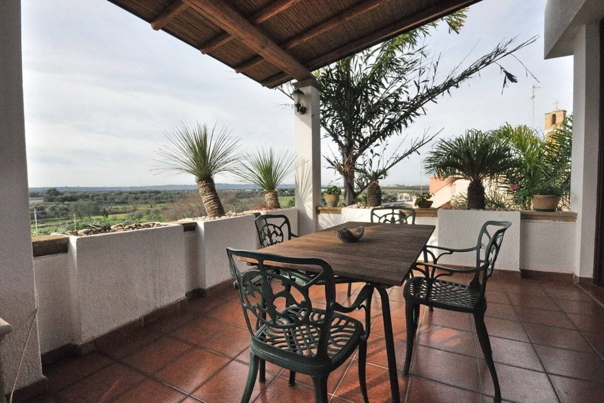Eine überdachte Terrasse mit Tisch und Stühlen, mit Blick auf eine Landschaft mit Bäumen und Gebäuden.