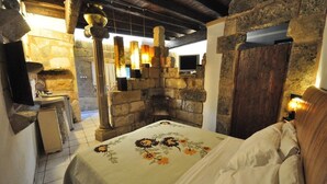A cozy room with a stone fireplace, a bed with floral bedding, and a stone wall. - Felline In B&B (Alliste)