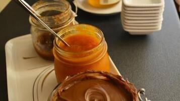 Una mesa con frascos de mermeladas y condimentos, incluyendo crema de chocolate y miel.