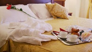 Ein ordentlich bezogenes Bett mit einem weißen Bademantel, einem Tablett mit Frühstücksgebäck und einer roten Rose auf dem Kopfkissen.