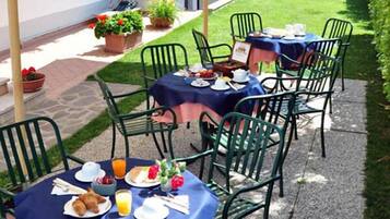 An outdoor dining area with tables and chairs, covered with blue tablecloths, and surrounded by potted plants.