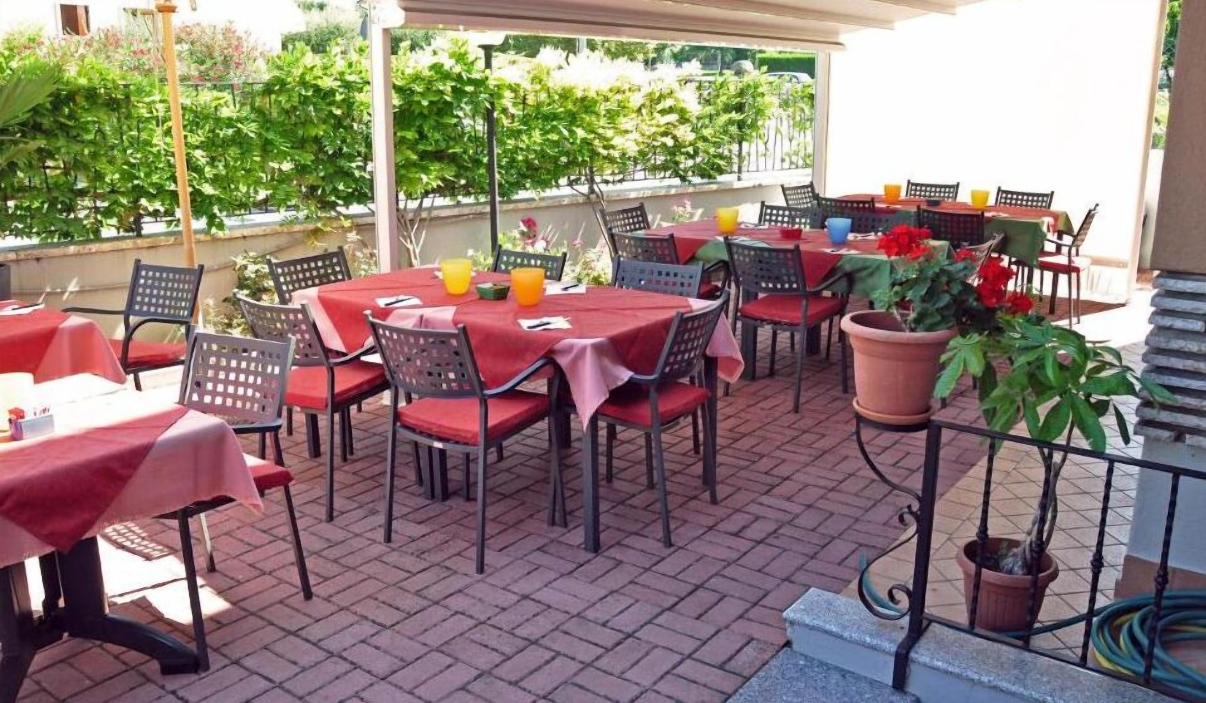 Un espace extérieur aménagé en terrasse, doté de plusieurs tables et chaises, abrité par un toit et entouré de verdure.
