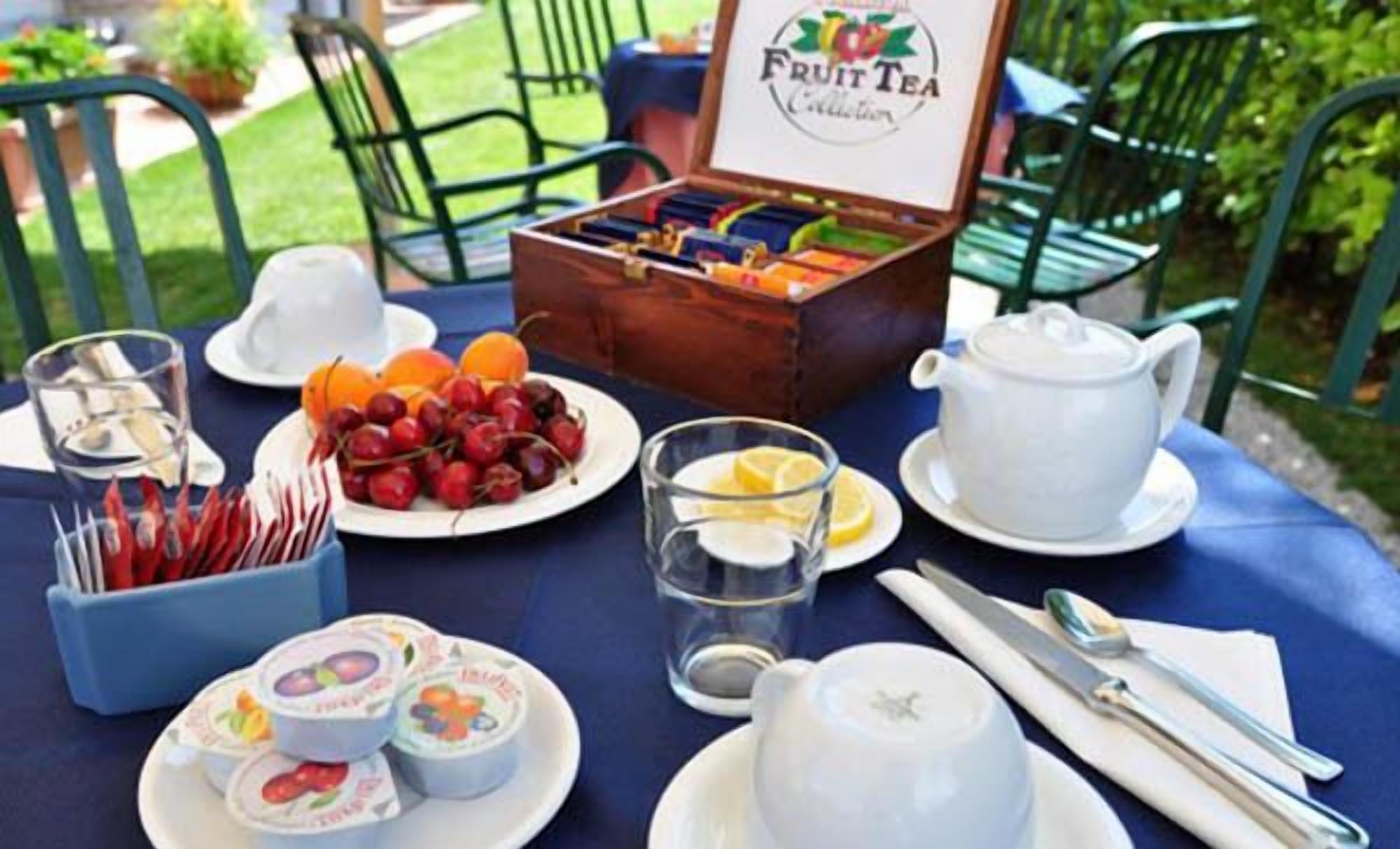 Una mesa lista para el desayuno, con un cartel de té de frutas, platos de fruta, una tetera y tazas.