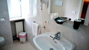 A bathroom with a sink, a hairdryer, a towel rack, a glass shelf with toiletries, and a window.