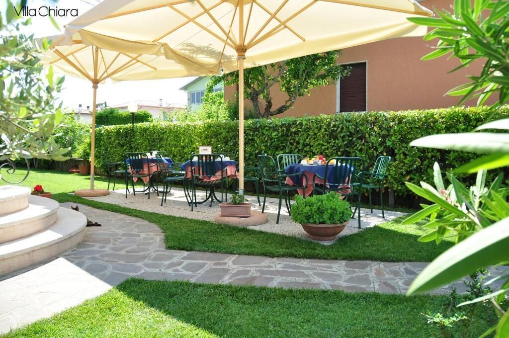 Un patio al aire libre con piso de piedra, sillas verdes y un paraguas grande.