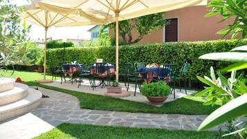 Un patio al aire libre con piso de piedra, sillas verdes y un paraguas grande.