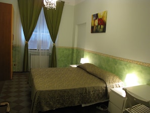 A bedroom with a bed, a bedside table, a lamp, a window with curtains, and a painting on the wall. - Claudia House Roma Termini (Rome)