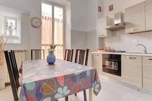 A modern kitchen with a dining table, chairs, a clock, and a window with curtains. - Claudia House Roma Termini (Rome)