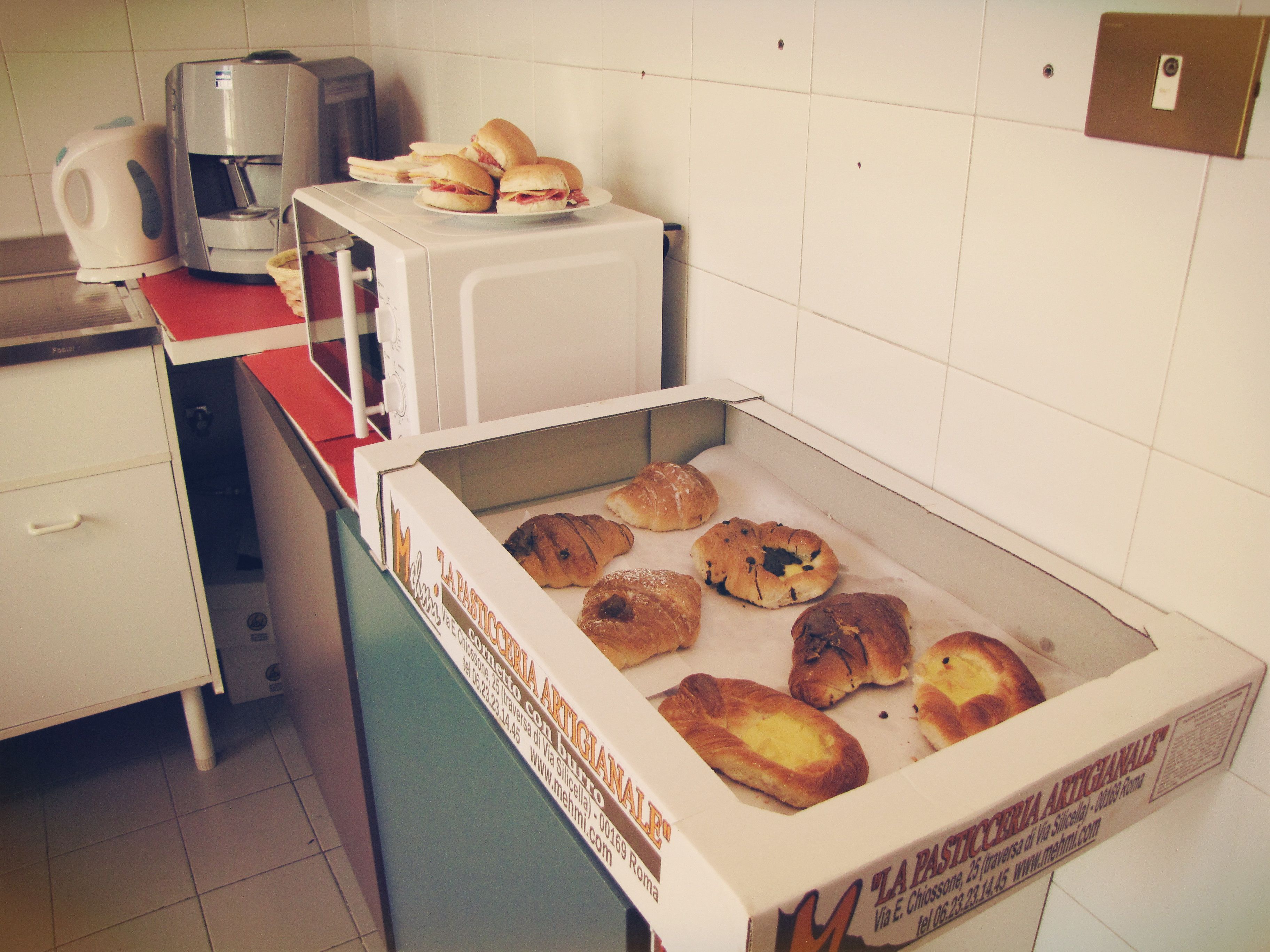 A kitchen with a coffee maker, a microwave, and a box of pastries.