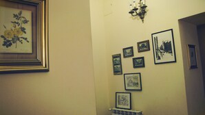 A hallway with framed pictures on the wall, a radiator, and a candelabra. - Claudia House Roma Termini (Rome)