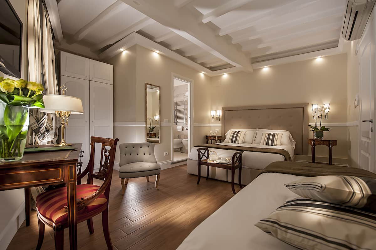 Ein Schlafzimmer mit Bett, Nachttisch, Lampe, Stuhl und Blick ins Badezimmer.