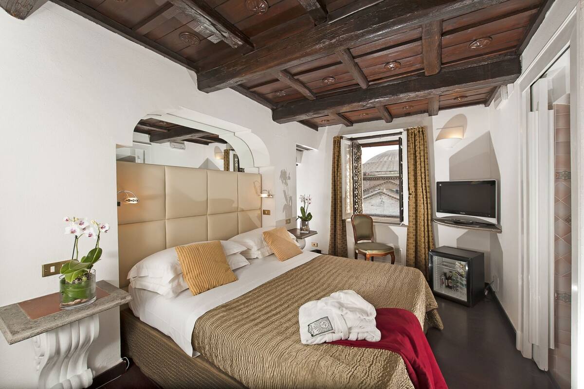 Ein Hotelzimmer mit einem großen Bett, einem Fernseher, einem Sessel und einem Fenster mit Vorhängen.