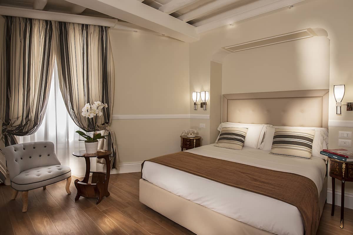 Ein Hotelzimmer mit einem großen Bett, einem Sessel, einem kleinen Tisch mit Pflanze und einem Nachttisch mit Lampe.