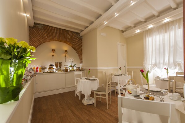 A dining area with tables set for breakfast, featuring a brick archway, white walls, and a window with sheer curtains. - La Residenza del Sole al Pantheon (Rome)