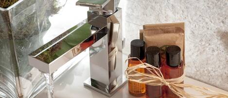 Un baño con un grifo moderno, un recipiente de vidrio con musgo y un conjunto de botellas de aceites esenciales atadas con un cordón.