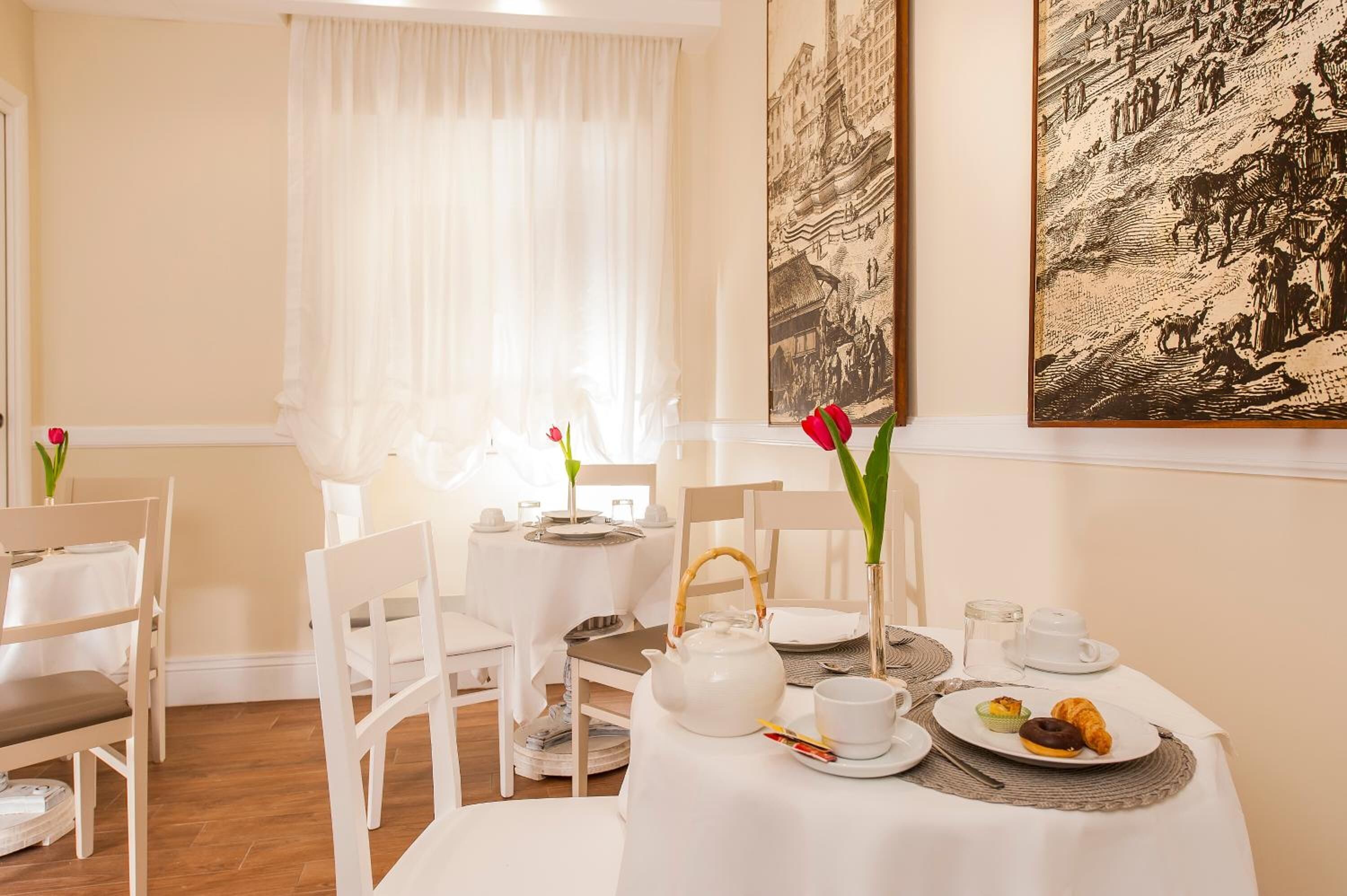 A dining area with white tables and chairs, a teapot, cups, and pastries.