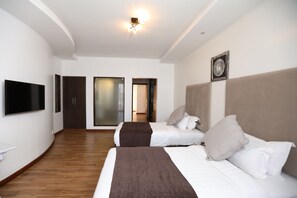 A hotel room with two beds, a flat-screen TV, a large mirror, and a sliding door leading to a bathroom. - Bidwood Suite Hotel (Nairobi)