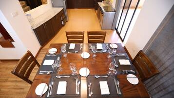 Comedor con mesa de madera preparada para seis personas, rodeado de sillas, en una cocina moderna con vista al área de estar.